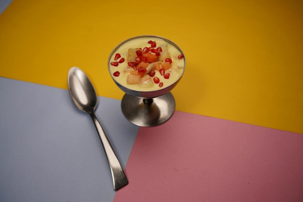 A delicious fruit dessert with pomegranate and papaya served in a metal cup on a colorful background.